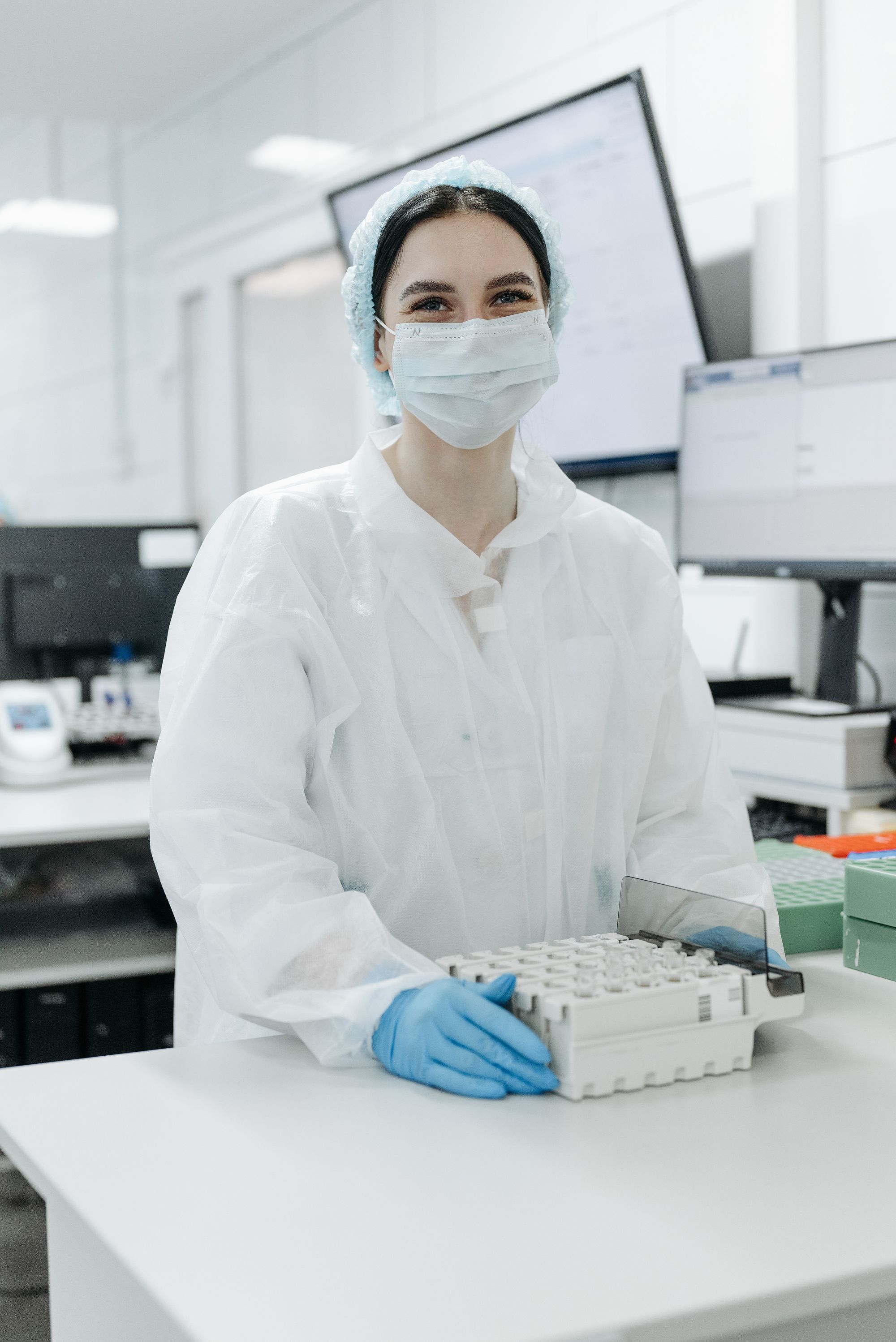A smiling lab technician in a mask and hairnet holding a sample rack
